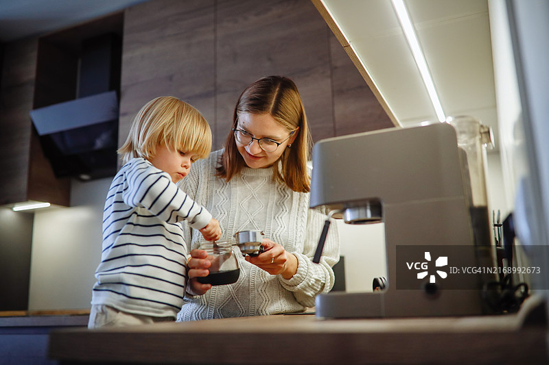家庭生活真实瞬间：母子在厨房用咖啡机一起煮咖啡，捕捉温馨真实的清晨体验图片素材