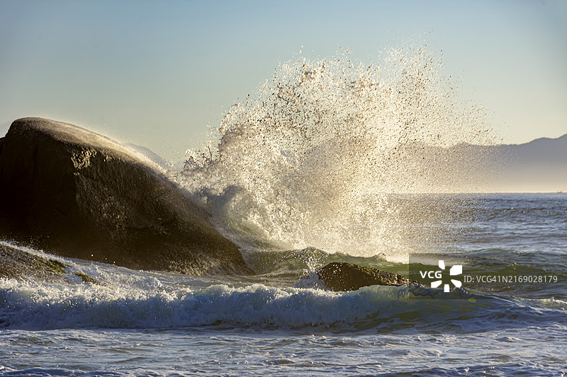 巴西里约热内卢伊帕内玛魔鬼海滩，夏日黎明时分海浪拍打着岩石，背景是群山图片素材