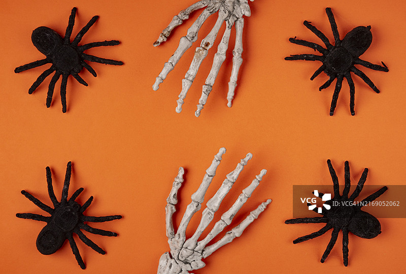 橙色背景上的黑色蜘蛛和骷髅手，万圣节图片素材