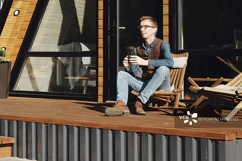 戴眼镜的中年男人坐在木屋的露台上图片素材