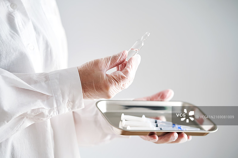 医生戴手套的手托着装有注射器和药剂的托盘图片素材