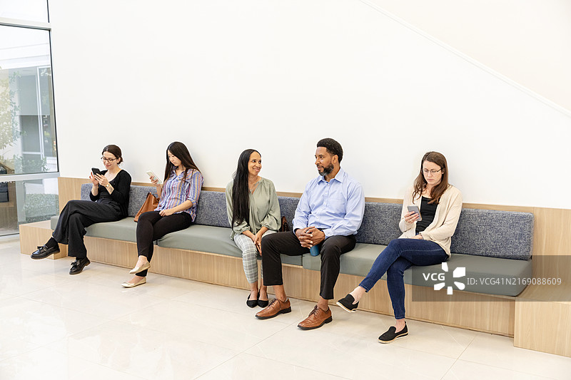 不同人群坐在建筑物中庭的墙边长椅上图片素材