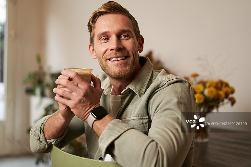 微笑的男人坐在家里拿着咖啡杯的肖像图片素材