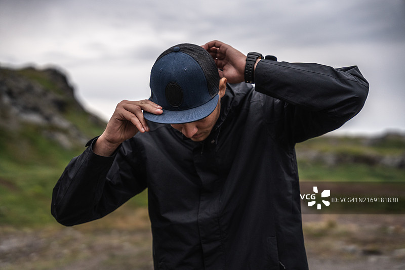 在山区调整棒球帽的年轻男子肖像，壮丽的景色图片素材