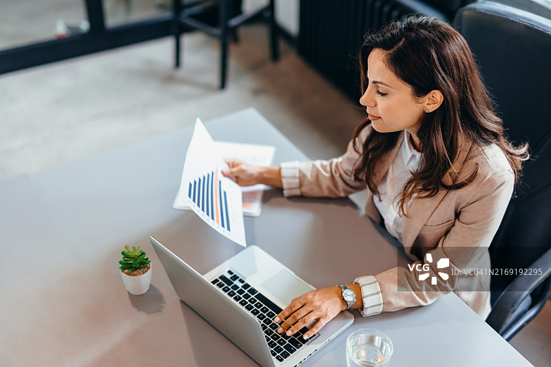 女商人在办公桌前用笔记本电脑和文件分析图表图片素材