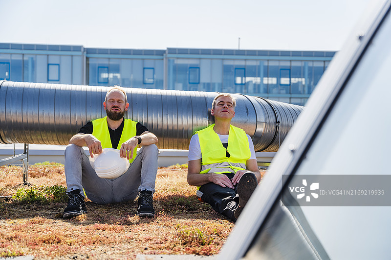 两名穿安全背心的工人在公司办公楼顶楼休息图片素材