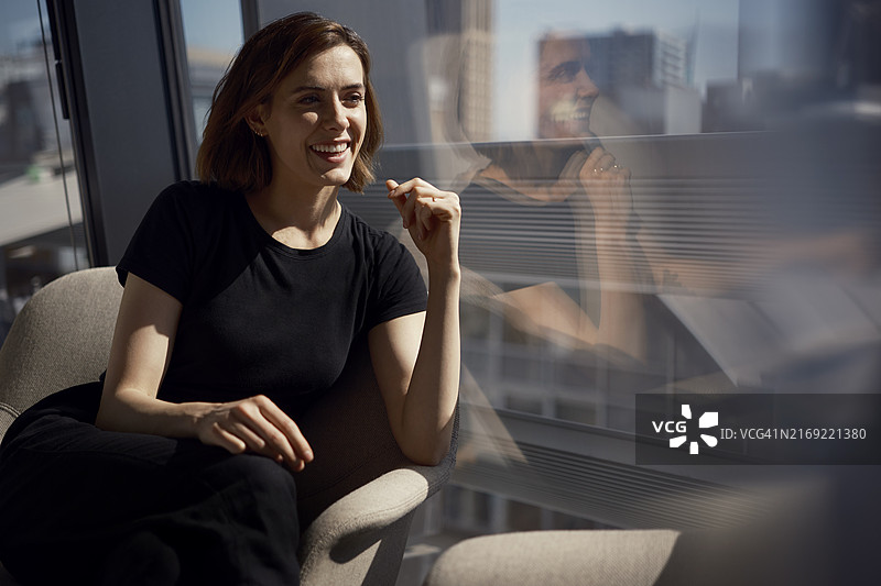 快乐的年轻女商人坐在办公室窗边的椅子上图片素材