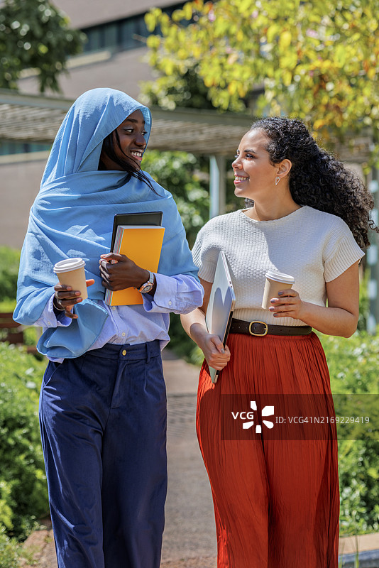 拿着咖啡杯在办公园区行走的微笑的多民族同事图片素材