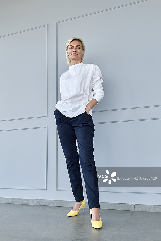 微笑女商人双手插兜站在墙前图片素材