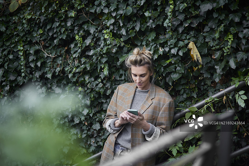 优雅女人在树篱旁使用手机图片素材