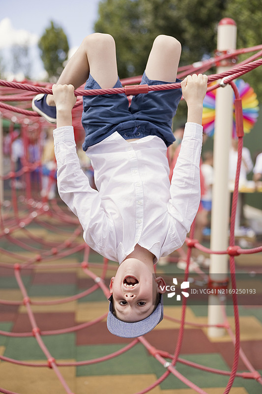 男孩在游乐场攀爬网上倒挂图片素材