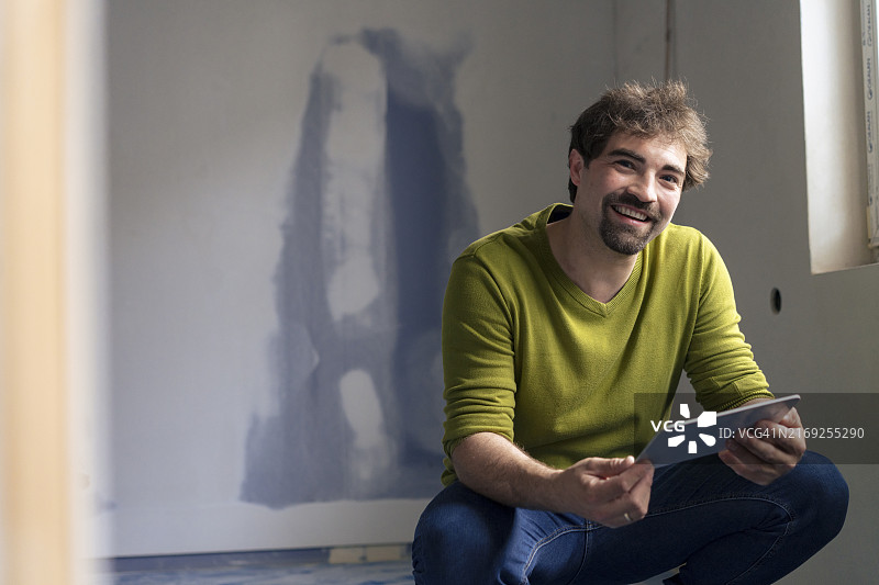 面带微笑的男人在新公寓里蹲着并拿着平板电脑图片素材