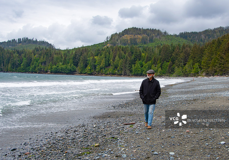 年长的男人在阴天的海滩上行走，加拿大不列颠哥伦比亚省温哥华岛图片素材