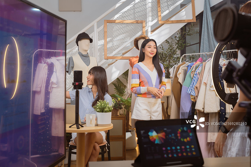 亚洲时尚女主播在直播间用手机直播卖衣服图片素材