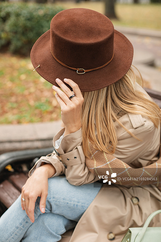 戴帽子穿冬季羊毛外套的时尚女人坐在白俄罗斯秋日阳光明媚的公园长椅上图片素材