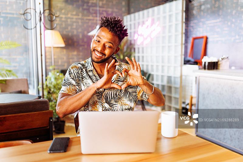 身材健壮的伊朗族男人用手指比心，在视频通话中看着笔记本电脑屏幕图片素材