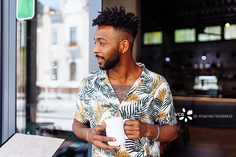在咖啡店门口喝咖啡的健壮的西亚裔创业者图片素材