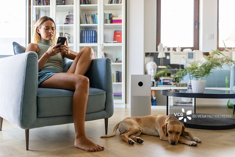 在客厅的扶手椅上放松并用手机打字的女人图片素材