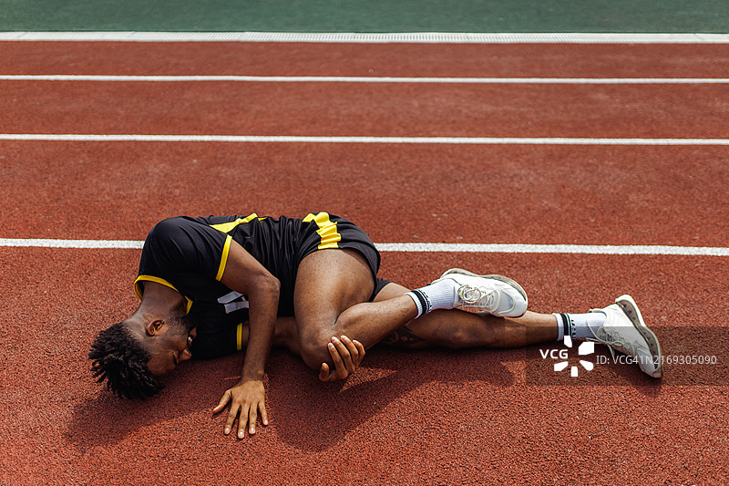 受伤的伊拉克运动员坐在跑道上，扶着膝盖感到疼痛图片素材