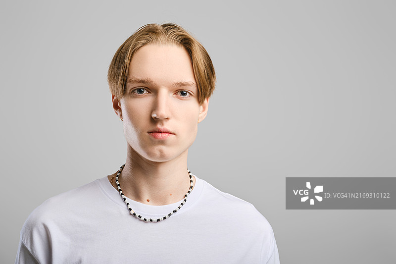 灰色工作室背景下，身穿白色T恤的严肃年轻男子特写图片素材