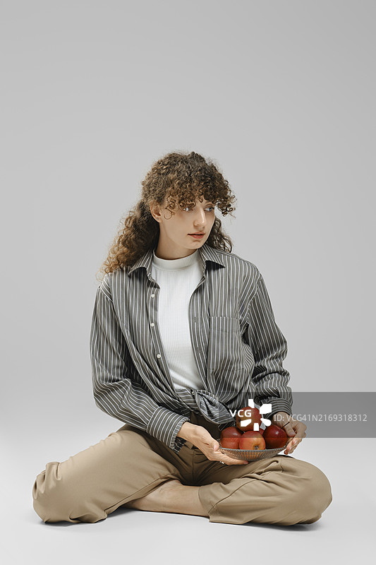 年轻女子坐在地上，膝盖上放着一碗苹果图片素材