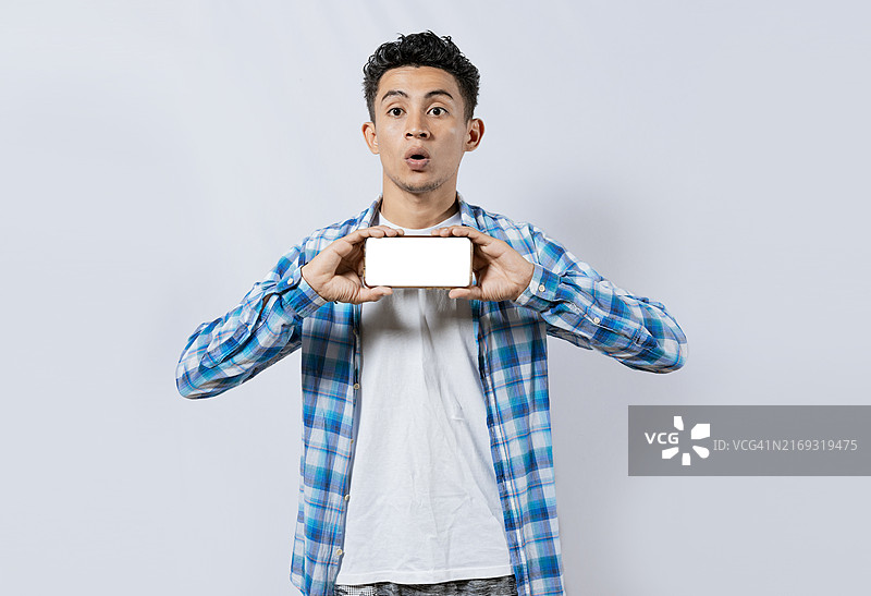 惊讶的年轻人用手机展示广告。惊喜的英俊男人展示手机的横向屏幕，戴眼镜的家伙展示智能手机的空白屏幕图片素材