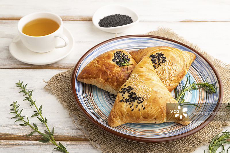 白色木质背景和亚麻纺织品上的自制亚洲萨摩萨三角饺与绿茶。侧视图图片素材