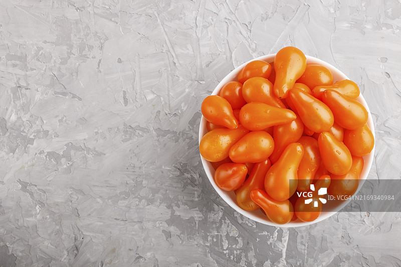灰色水泥背景白色陶瓷碗中的鲜橙葡萄小番茄图片素材