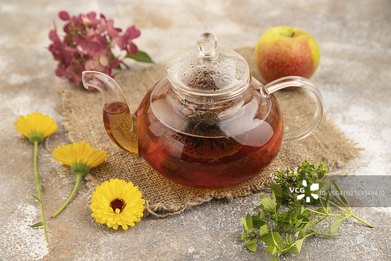 棕色水泥背景和亚麻纺织品上的玻璃茶壶草本红茶。健康饮品概念，侧视特写图片素材
