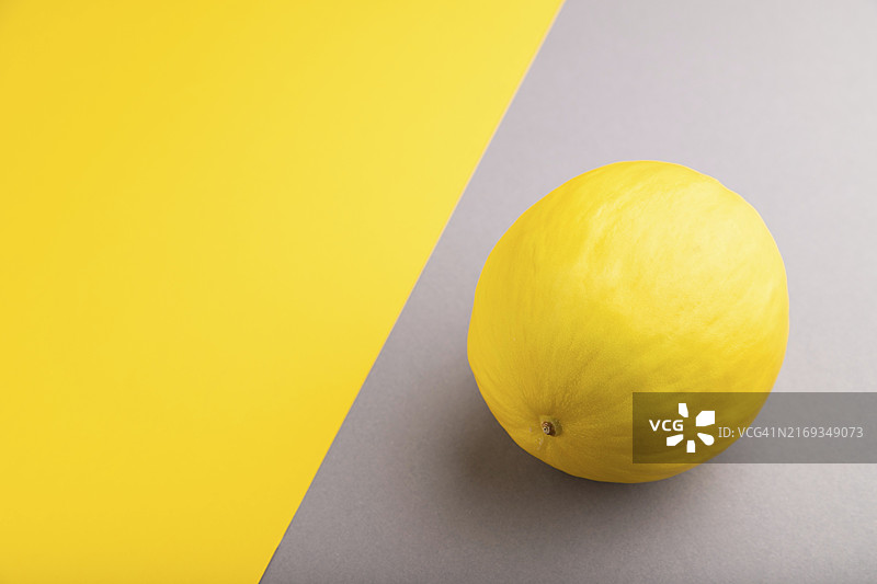 成熟的黄色甜瓜，在灰色和黄色粉彩背景上。侧视图，留有文字空间。收获、健康、纯素食品概念，极简主义图片素材