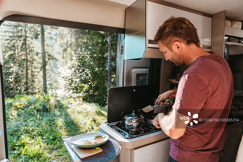 男人在有森林景观的露营车内做早餐图片素材