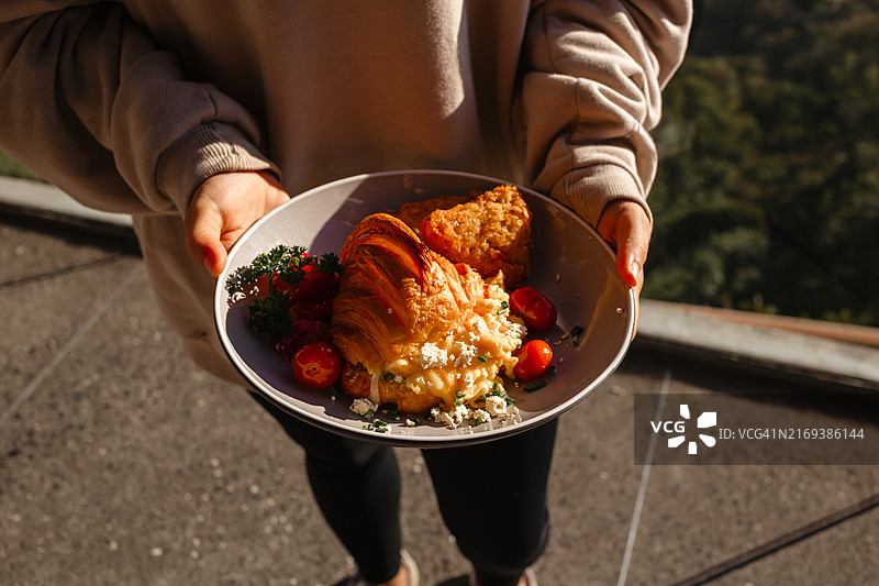 女人手拿夹着煎蛋卷和奶酪的羊角面包，时尚早餐概念图片素材