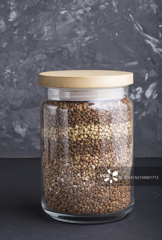 黑色水泥背景分层倒入荞麦的玻璃罐，侧视图，特写，健康食品概念图片素材