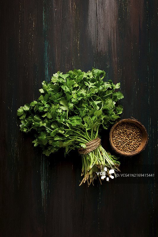深色木桌上的新鲜香菜和芫荽籽图片素材