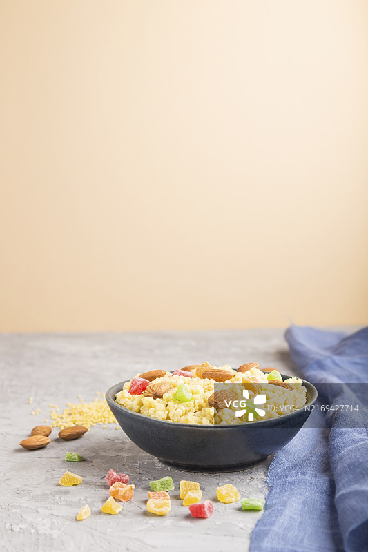 灰色和橙色背景蓝色陶瓷碗中，以及蓝色亚麻纺织品上的蜜饯果脯杏仁小米粥。侧视图，特写，选择性聚焦，留白图片素材