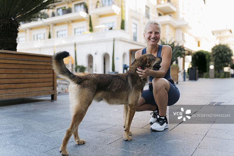 清晨慢跑时，充满活力的女人在城市街道上爱抚着小狗图片素材