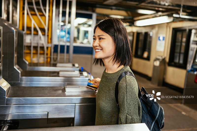 亚洲女性在地铁站使用卡通过旋转栅门，身穿休闲服装，背着背包图片素材