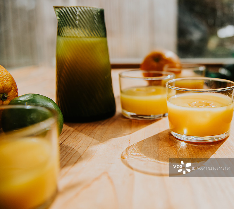 阳光明媚的早晨，木桌上放着一小壶橙汁和新鲜柑橘果汁图片素材