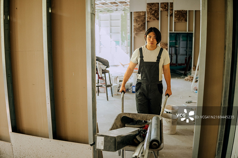 年轻的男性建筑工人在建筑工地使用建筑手推车图片素材