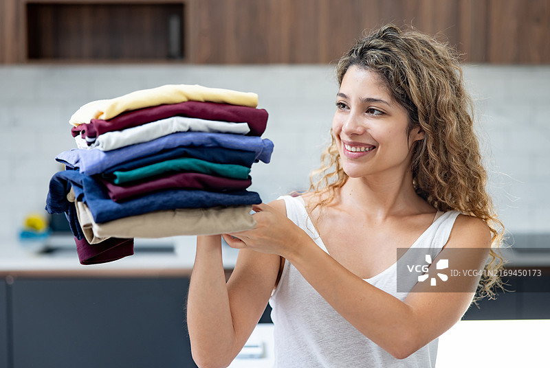 快乐的女人在洗衣服，手里拿着一堆衣服图片素材