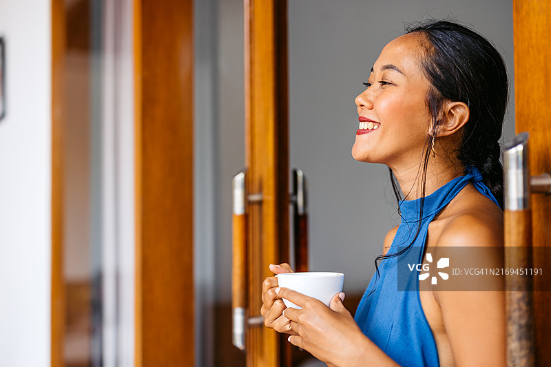 年轻的亚洲女性在印度尼西亚巴厘岛的别墅露台上喝咖啡图片素材