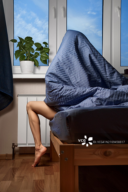 女子裹着毯子坐在床上，望着窗外图片素材