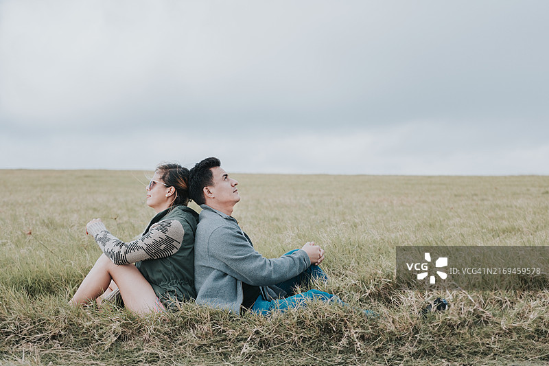 情侣在田野里背靠背坐着看天空图片素材