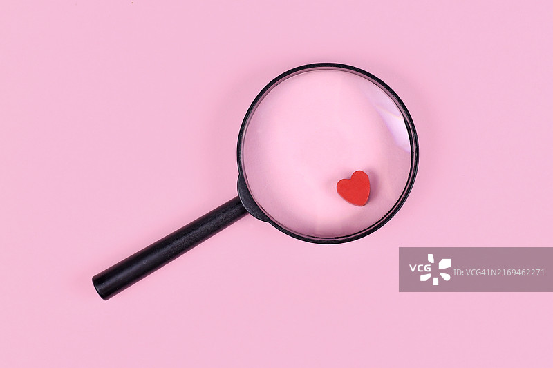 用放大镜和红色心形图标在粉红色背景上寻找爱情的概念图片素材