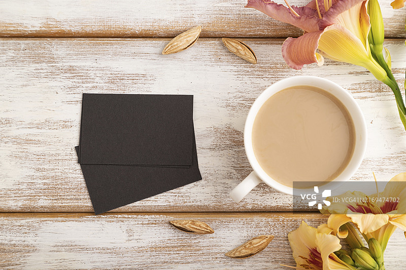 黑色纸质名片样机，搭配橙色萱草花和咖啡杯，白色木质背景。留白，俯视，扁平风格，复制空间，静物。春季概念图片素材