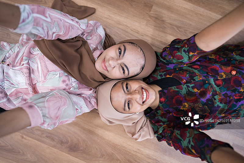 两名戴着头巾、穿着颜色鲜艳的衣服的微笑女人躺在木地板上，抬头看着镜头图片素材