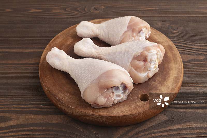 棕色木质背景木制砧板上的生鸡腿特写侧视图图片素材