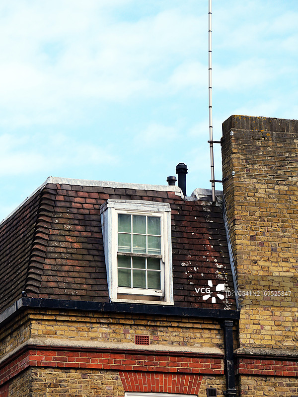 伦敦,英格兰,英国一座老旧黄砖房屋的棕色瓦屋顶特写,配有窗框。阳光和天空。自然色彩和风化效果。图片素材