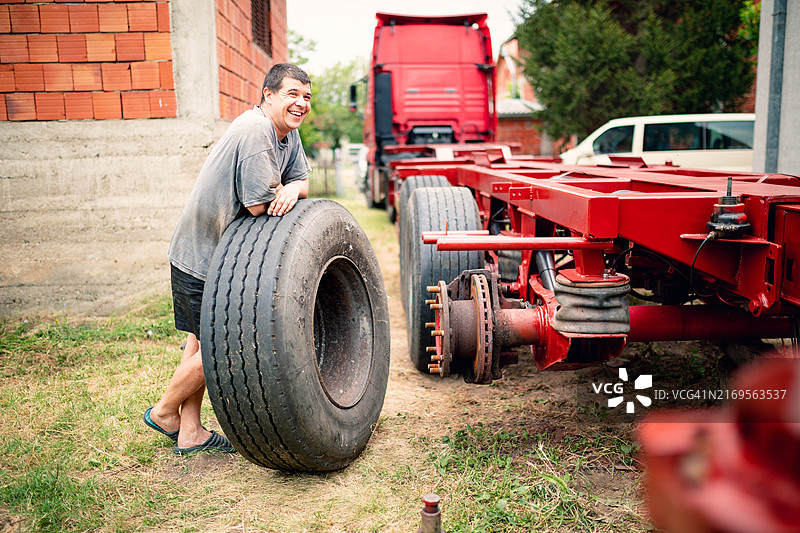 男人靠在卡车轮胎上，准备将其装回拖车图片素材