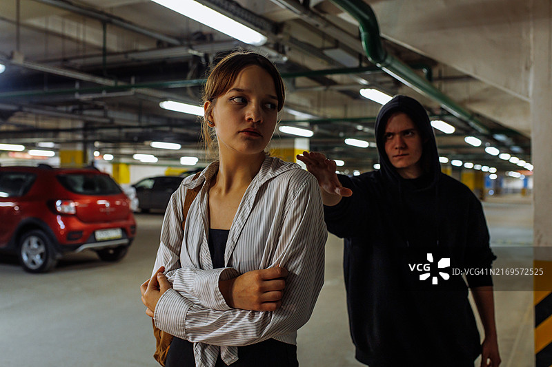 在地下停车场，一个穿黑色连帽衫的阴沉年轻人跟踪一个年轻女子图片素材